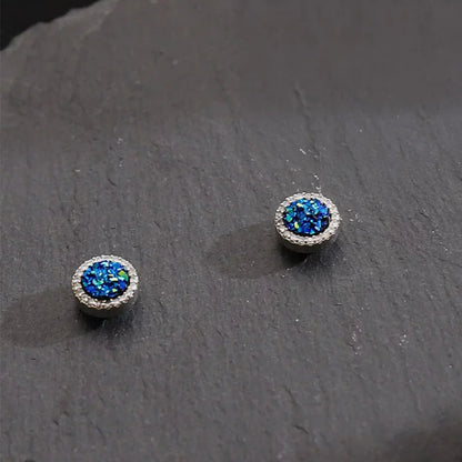 A pair of Nova Iridescent Blue Galaxy Magnetic Stud Earrings, showcasing their sparkling blue druzy texture on a dark slate background.