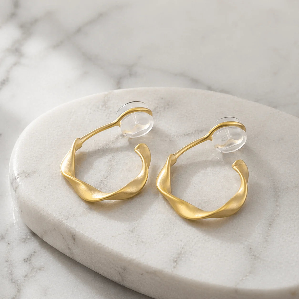 Matte gold organic abstract clip on earrings resting elegantly on a marble surface.