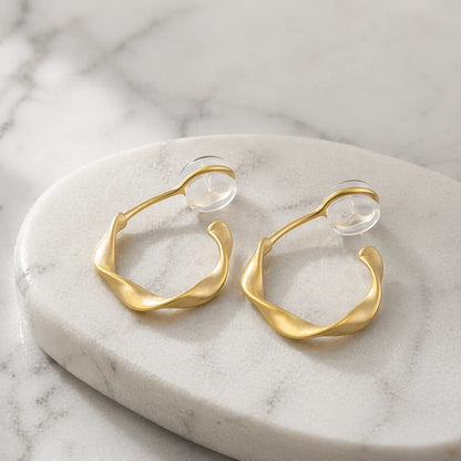 Matte gold organic abstract clip on earrings resting elegantly on a marble surface.