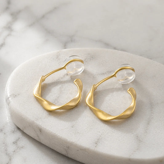 Matte gold organic abstract clip on earrings resting elegantly on a marble surface.