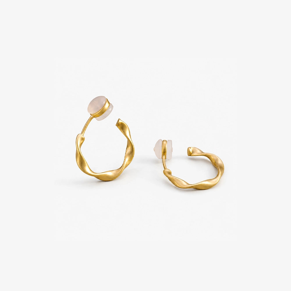 A diagonal view of matte gold sculptural clip on hoop earrings, showing the comfort pad and c-type clip on closure detail.
