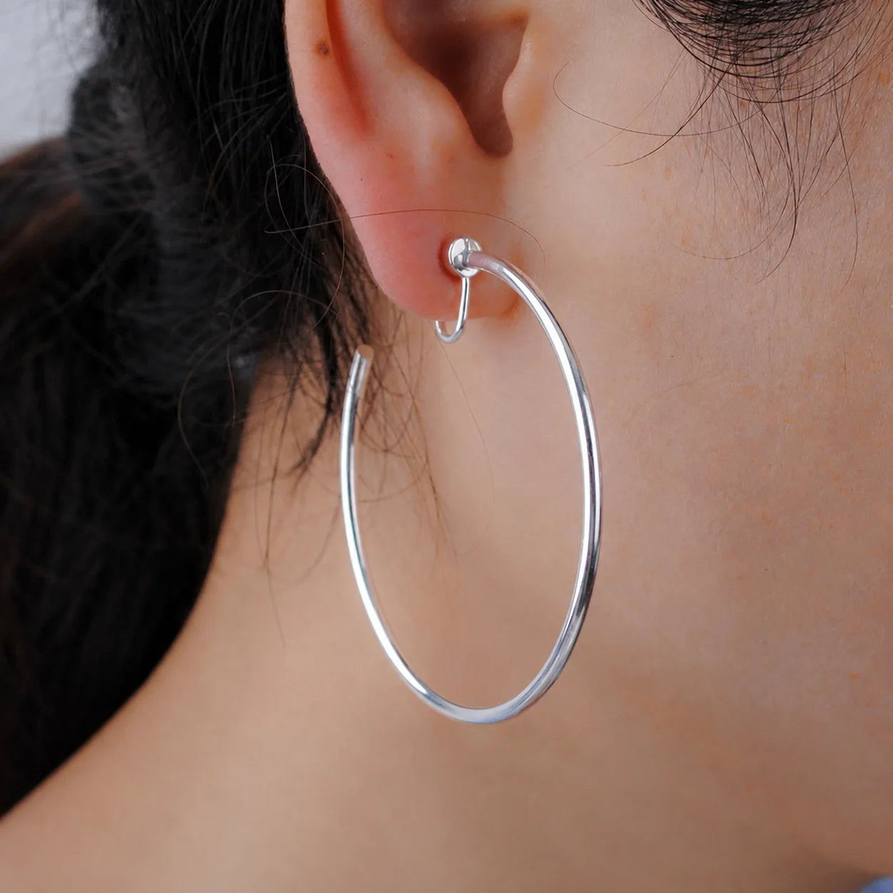 Oversized thin hoop clip-on earring worn on a non-pierced ear, shown in the silver-tone finish