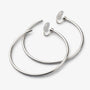 Pair of large silver-tone hoop clip-on earrings lying flat on a light gray background