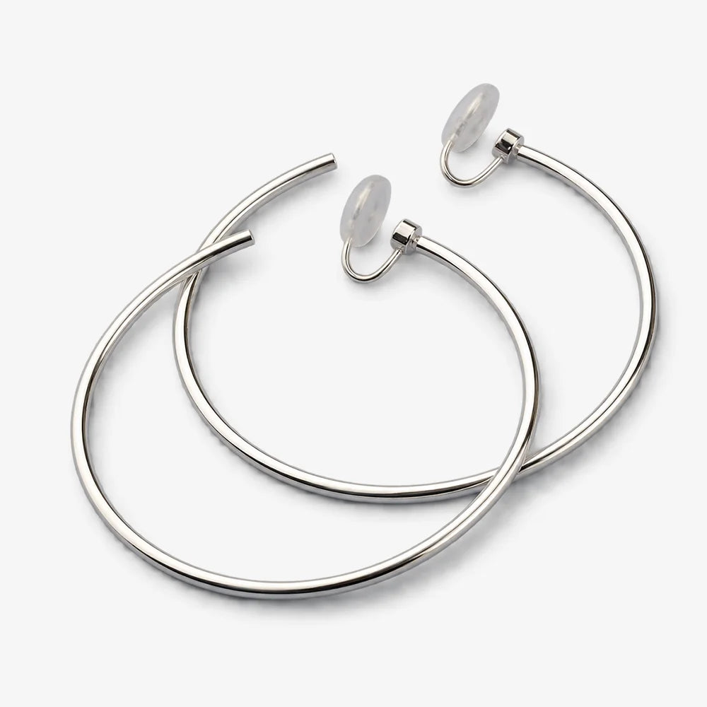 Pair of large silver-tone hoop clip-on earrings lying flat on a light gray background