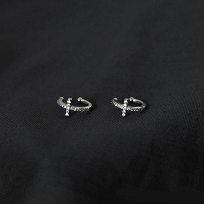 A pair of pavé silver cross clip-on cartilage cuffs, showcasing their sparkling details on a dark background.