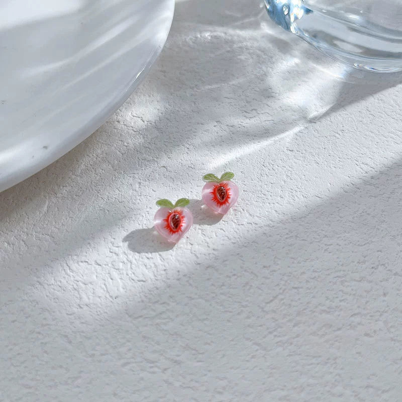 Two sweet peach magnetic clip-on earrings resting on a white textured surface under soft sunlight, showing the translucent jelly-like resin texture.