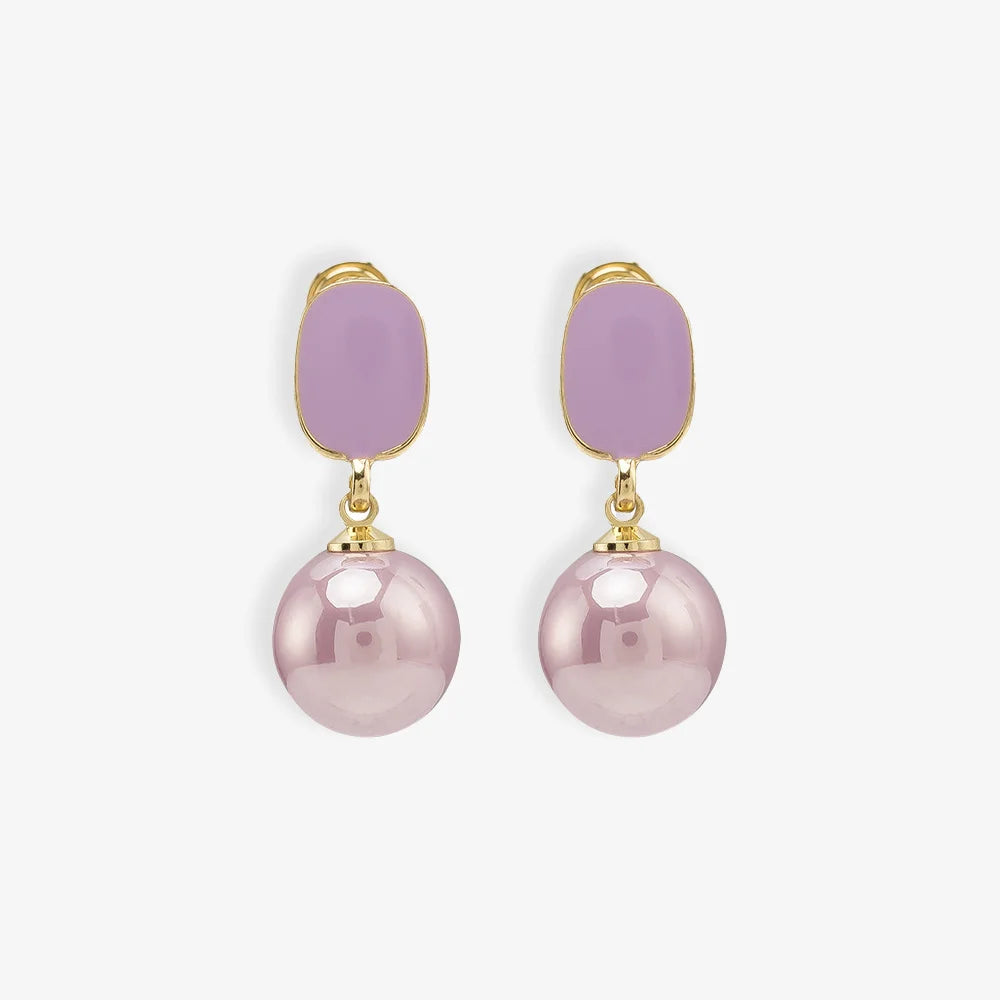 Pair of Purple Pearl Clip-On Drop Earrings displayed on a soft beige surface, capturing the elegant design and color contrast.