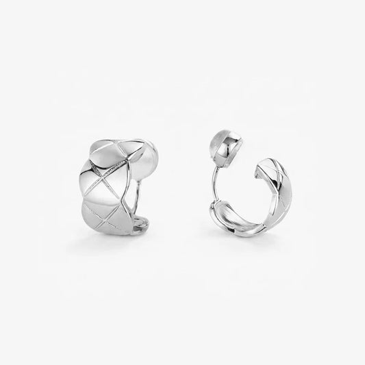 Front view of a pair of quilted silver huggie clip on earrings showing the textured diamond pattern.