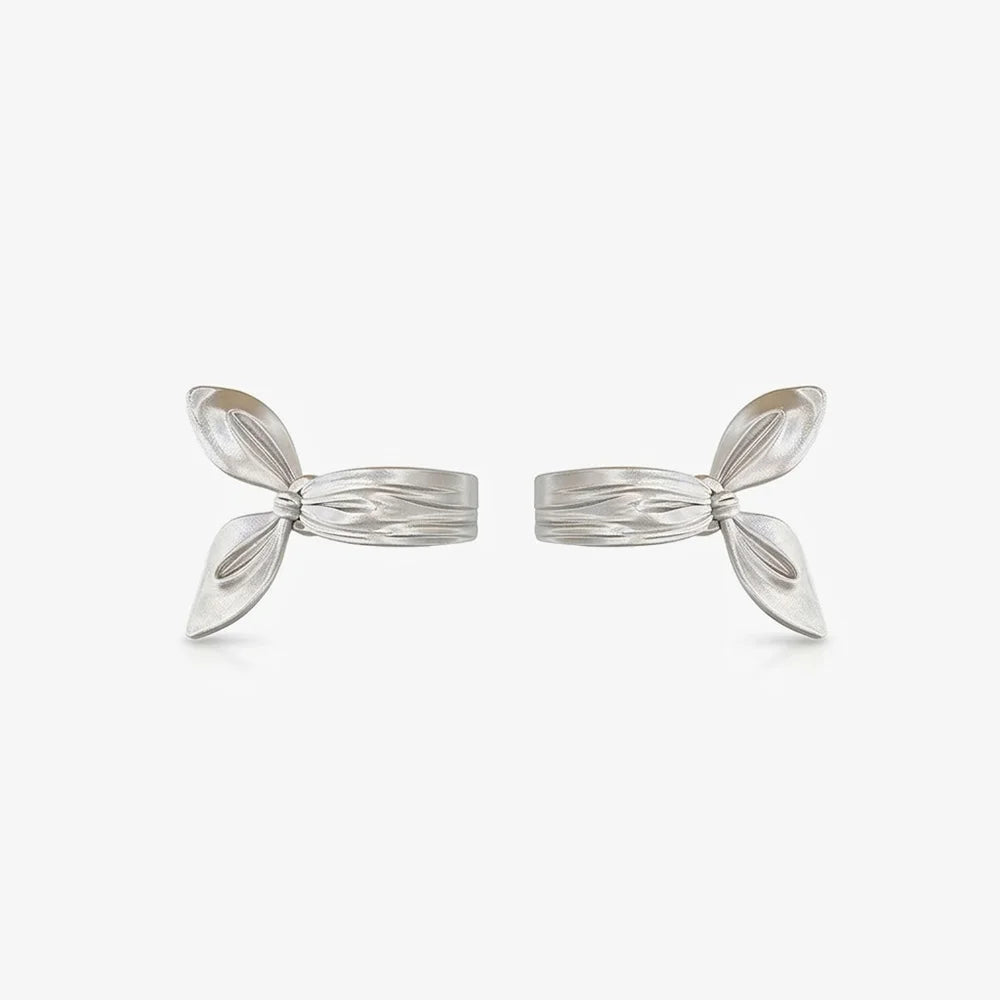 A pair of sculptural radiant silver-plated clip-on earrings designed to look like a thick ribbon bow ear cuff, isolated on a white background.
