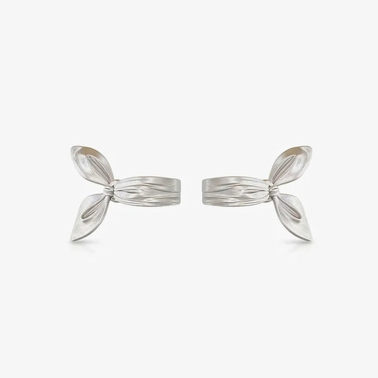 A pair of sculptural radiant silver-plated clip-on earrings designed to look like a thick ribbon bow ear cuff, isolated on a white background.