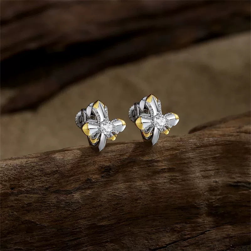 Regal two-tone cross clip-on earrings with gold accents and a CZ center stone, displayed on a dark wooden background.