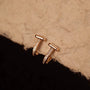 Rose gold earrings with small diamonds on a textured beige surface