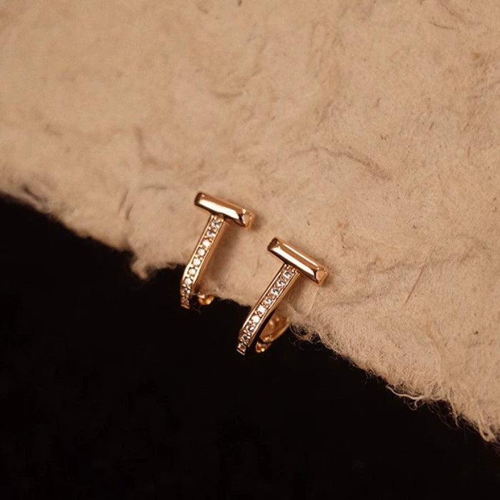 Rose gold earrings with small diamonds on a textured beige surface