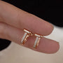 Rose gold earrings with small diamonds T-motif design on a finger against a neutral background