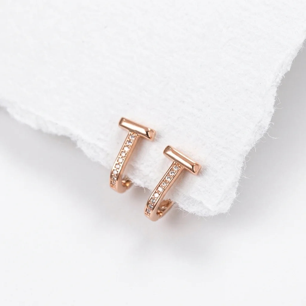 A pair of rose gold huggie hoop earrings with pavé-set clear stones, displayed on a textured white paper towel corner against a white background.