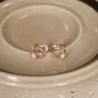 Elegant rose gold twisted circle stud earrings featuring a single brilliant-cut solitaire diamond accent on a ceramic dish.