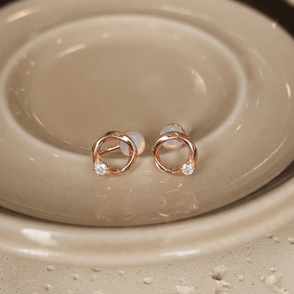 Elegant rose gold twisted circle stud earrings featuring a single brilliant-cut solitaire diamond accent on a ceramic dish.