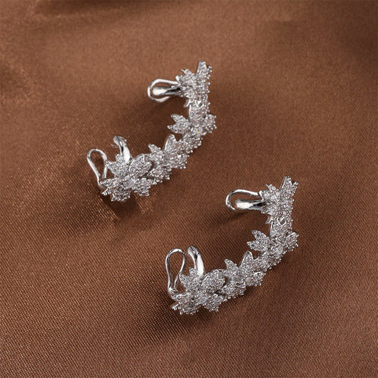 White gold Blossom Flower Crystal Helix Ear Cuffs resting on brown fabric, displaying the delicate craftsmanship of the flower-inspired design with zircon gems, embodying natural beauty for special occasions.