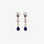 A pair of rose gold clip-on earrings featuring a large navy blue teardrop sapphire and a sparkling crystal starburst accent on a clean white background.