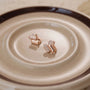 Rose gold earrings with clear stones on a beige plate, designed as pill-shape