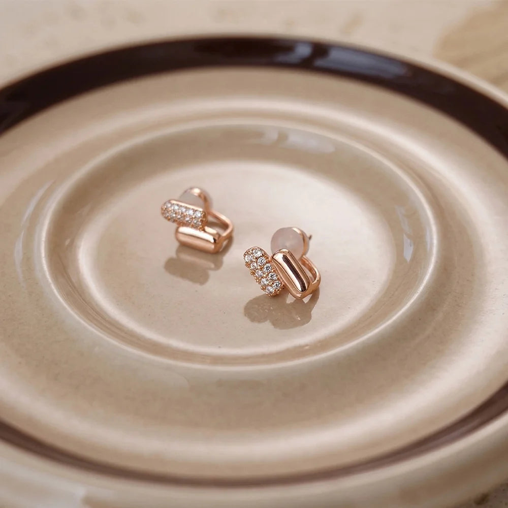 Rose gold earrings with clear stones on a beige plate, designed as pill-shape