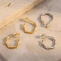A pair of matte gold sculptural clip on hoop earrings and a pair of matte white gold sculptural clip on hoop earrings shown together on marble surface.