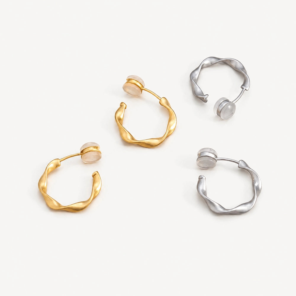 A pair of matte gold sculptural clip on hoop earrings and a pair of matte white gold sculptural clip on hoop earrings shown together on marble surface.