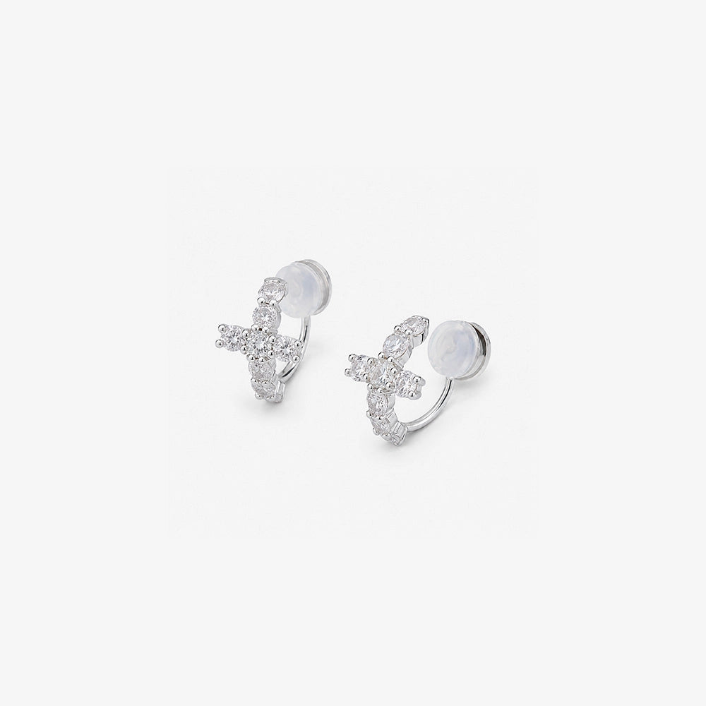 Angled detail of the cushioned clip on closure and pavé cross on silver huggie earrings