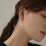 A close-up of a woman's ear wearing a delicate silver huggie hoop earring with three small stacked silver disc charms.