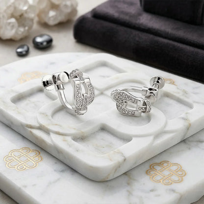 The Silver Pave Horseshoe Clip On Earrings displayed on a white marble jewelry tray, showcasing the high-shine finish and elegant horseshoe shape.