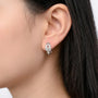 Un mannequin portant les boucles d'oreilles à clip en forme de fer à cheval pavées d'argent, démontrant comment le système de fermeture à vis imite un véritable piercing au lobe de l'oreille.
