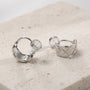 Close-up of silver quilted clip on earrings on a stone surface showing the open c-type clip on and comfort pad.