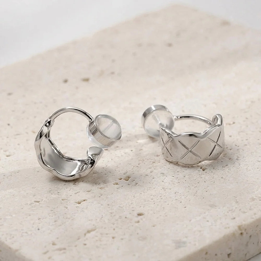 Close-up of silver quilted clip on earrings on a stone surface showing the open c-type clip on and comfort pad.