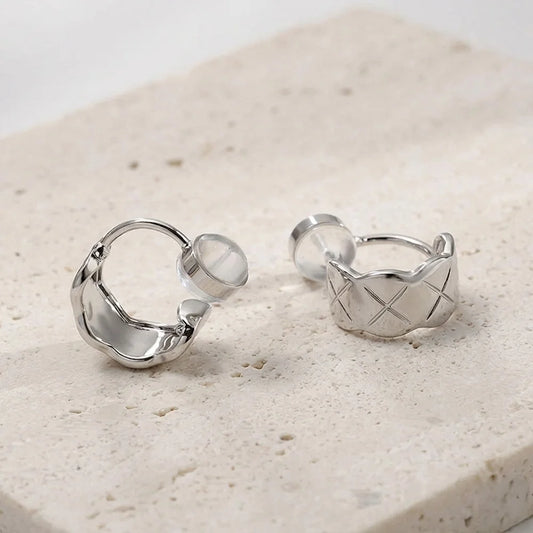 Close-up of silver quilted clip on earrings on a stone surface showing the open c-type clip on and comfort pad.