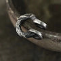 A detailed close-up of a single hammered oxidized silver ear cuff, highlighting the intricate texture and rugged appeal against a blurred background.