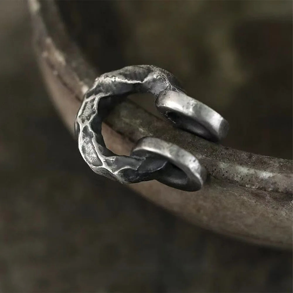 A detailed close-up of a single hammered oxidized silver ear cuff, highlighting the intricate texture and rugged appeal against a blurred background.