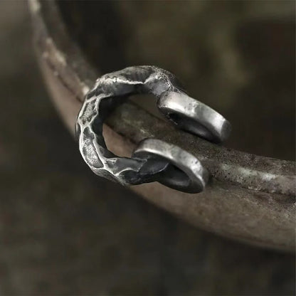 A detailed close-up of a single hammered oxidized silver ear cuff, highlighting the intricate texture and rugged appeal against a blurred background.
