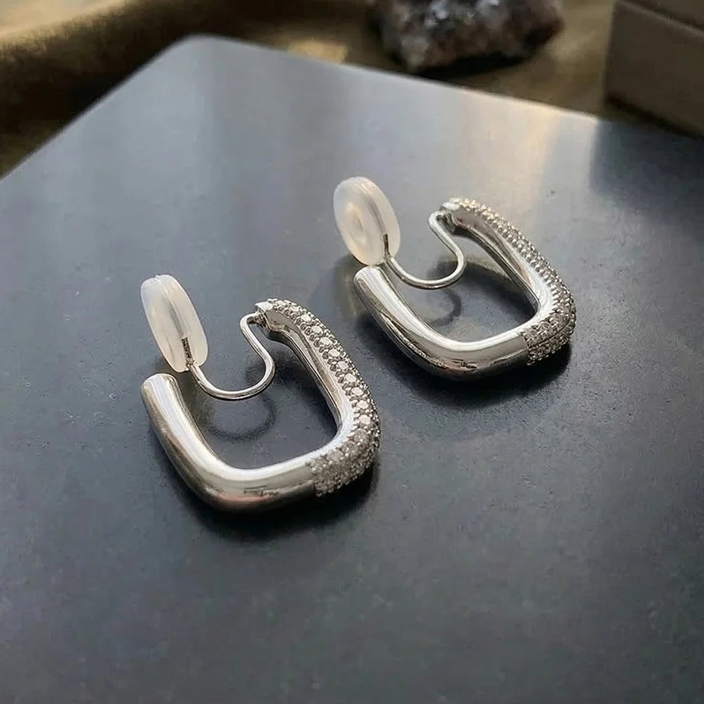 Close-up of the silver pave square-edge clip-on earrings on a dark grey stone surface, focusing on the intricate micro-pave setting.