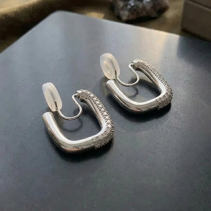 Close-up of the silver pave square-edge clip-on earrings on a dark grey stone surface, focusing on the intricate micro-pave setting.