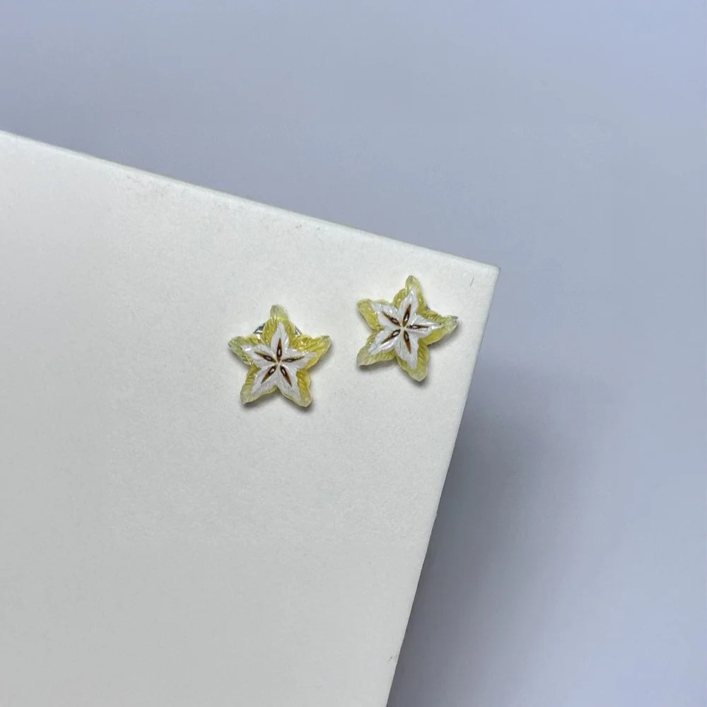 A pair of Tropical Star Fruit Magnetic Stud Earrings, featuring realistic yellow carambola slice designs, resting on a white card at an angle.