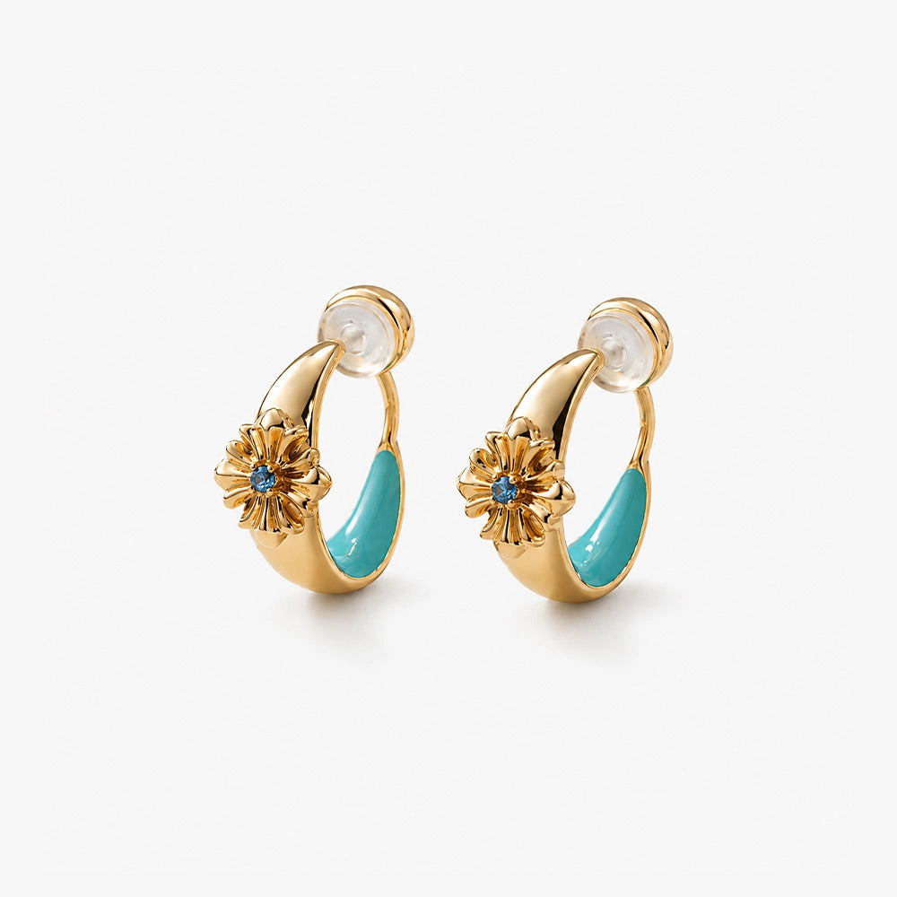 Close-up of turquoise enamel and gold bohemian ear clips on a natural stone surface showing the intricate cross design.