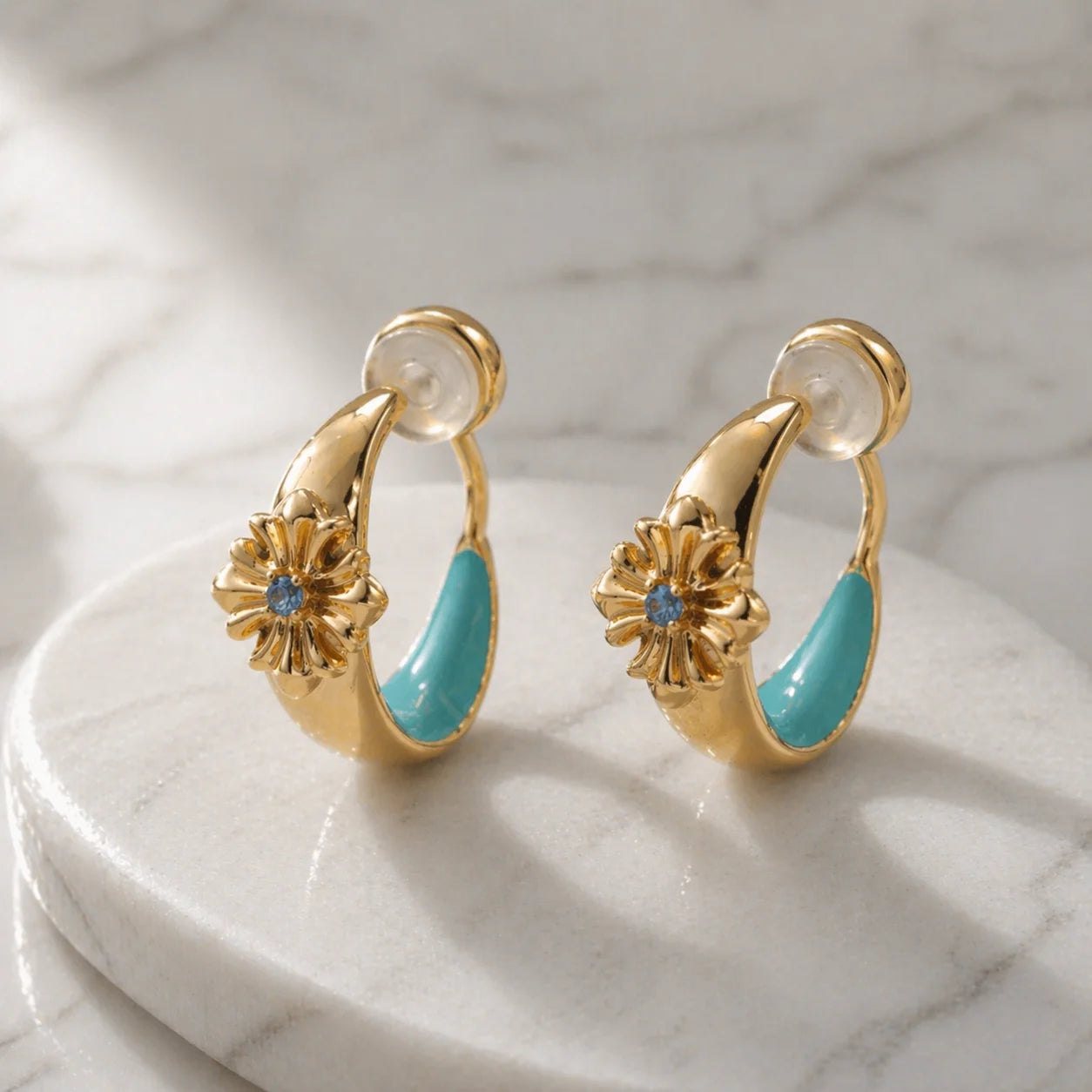 Close-up of turquoise enamel and gold bohemian ear clips on a natural stone surface showing the intricate cross design.