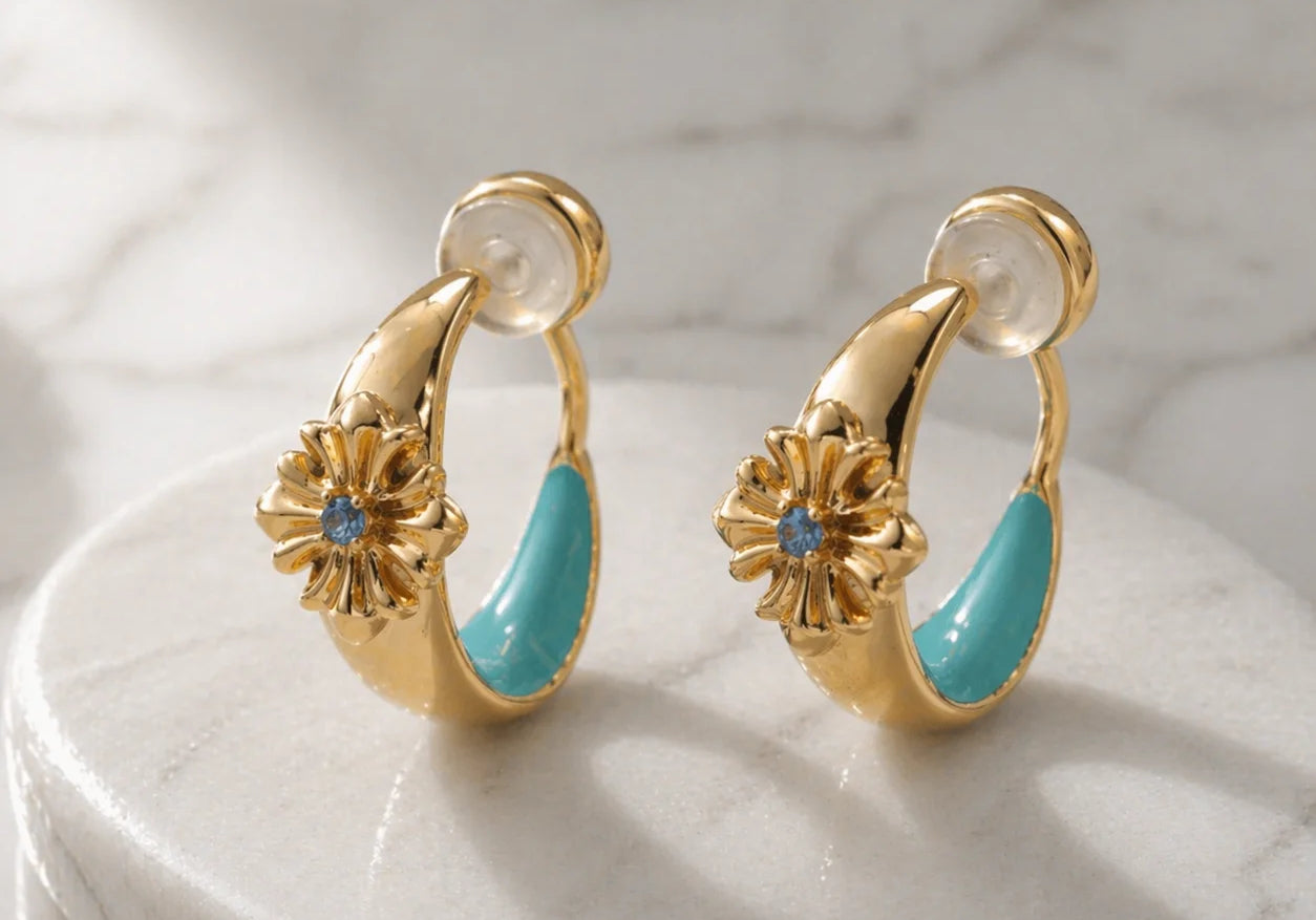Close-up of turquoise enamel and gold bohemian ear clips on a natural stone surface showing the intricate cross design.