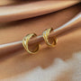 Vue latérale des boucles d'oreilles à clip en forme de C torsadées en or, mettant en valeur leurs couches sculptées et leur finition polie sur une surface satinée.