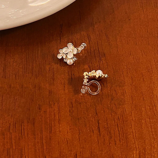 A close-up of the White Blossom Pearl invisible clip-on earrings, highlighting the detailed floral enamel, luminous fake pearls, and clear resin clip mechanism.