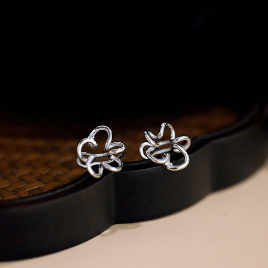 Elegant Cherry Blossom Floral Helix Ear Cuffs in white gold, resting on a dark traditional container, their Sakura-shaped design highlighted by the intricate craftsmanship and central zircon accent.