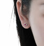 A close-up of a person's ear wearing a small silver-toned starburst stud earring with a red gemstone center.