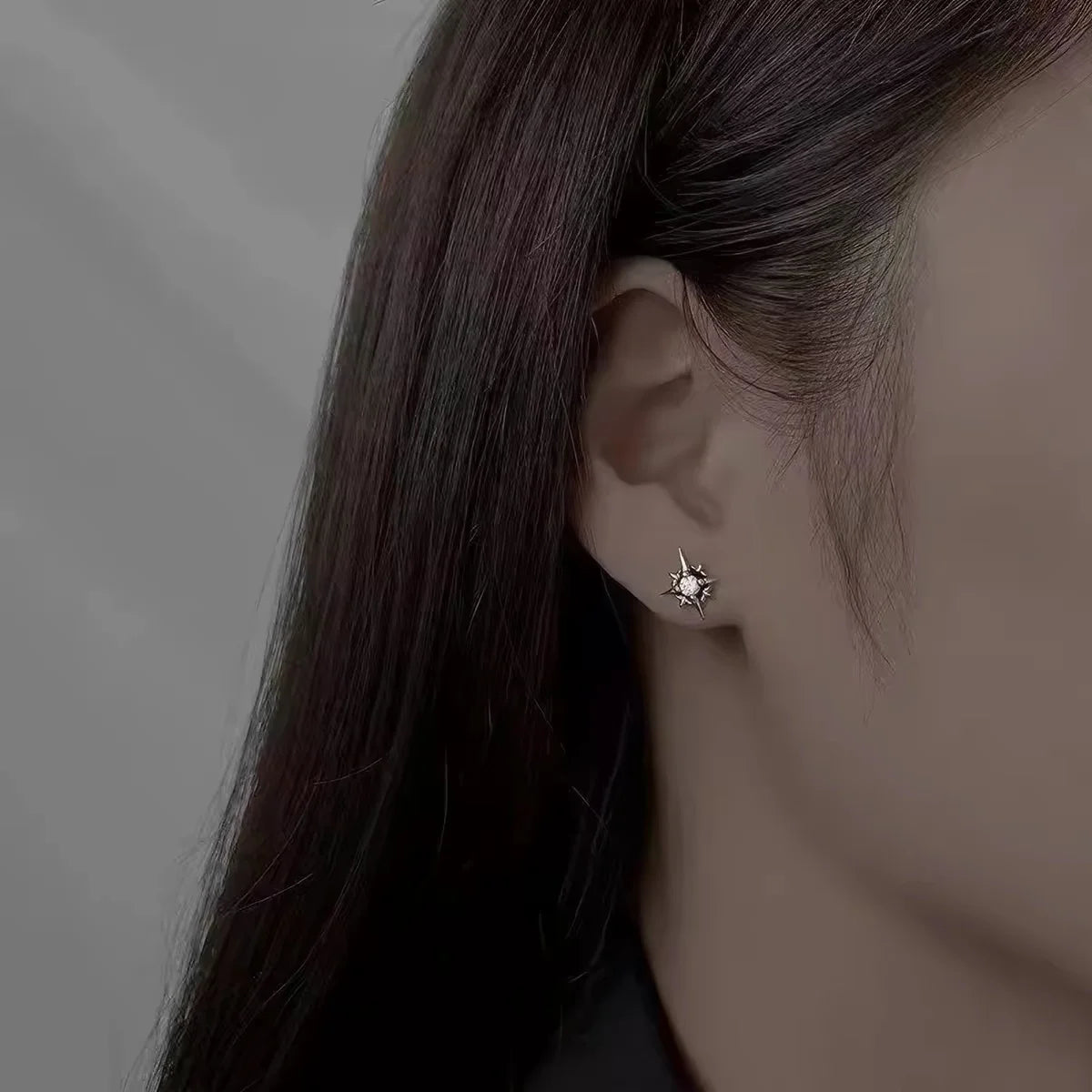 A close-up side profile of a woman wearing a small silver star-shaped stud earring with a clear gemstone.