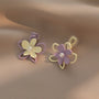 Pastel Petals Mismatched Clip-On Earrings in purple and cream displayed on beige fabric background