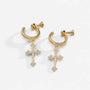 A pair of gold huggie hoop earrings with dangling cross charms, embellished with small clear pavé stones, shown on a clean white background.